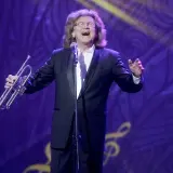 Zbigniew Wodecki w garniturze, z trąbką w dłoni, śpiewa na scenie. Jego utwory wciąż poruszają serca.