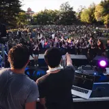 DJ-e tworzą atmosferę deep house na koncercie plenerowym. Tłum bawi się przy muzyce.