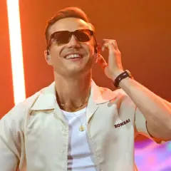Uśmiechnięty artysta w okularach przeciwsłonecznych, przygotowujący się do mrozu koncerty 2026.
