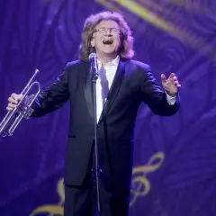 Zbigniew Wodecki w garniturze, z trąbką w dłoni, śpiewa na scenie. Jego utwory wciąż poruszają serca.