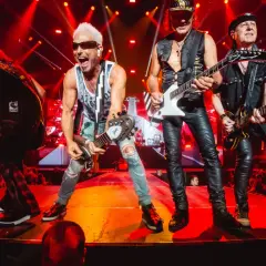 Scorpions na żywo, grając swoje legendarne utwory. Energetyczny koncert z czerwonymi światłami i tłumem fanów.