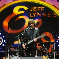 Jeff Lynne z Electric Light Orchestra na scenie, wykonuje swoje kultowe utwory. W tle logo zespołu.