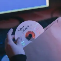Ręce wsuwają płytę CD z napisem "Simon Green" do brązowej koperty. Może to być bootleg muzyczny.