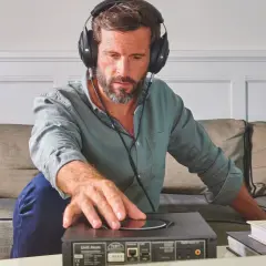 Mężczyzna w słuchawkach dotyka urządzenia audio, sprawdzając jego impedancję słuchawek.