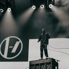 Tyler Joseph z Twenty One Pilots na scenie w Łodzi, w charakterystycznym stroju, na tle logo zespołu.