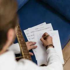 Mężczyzna z gitarą pisze tekst piosenki, tworząc nową wersję melodii.