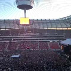 Ogromny tłum ludzi na koncercie na Narodowym. Widać scenę, telebimy i trybuny wypełnione widzami.