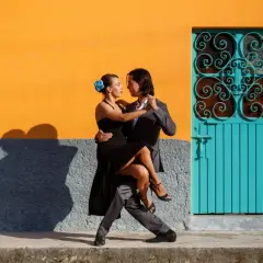 Para tańczy cha cha przy pomarańczowej ścianie i turkusowych drzwiach.