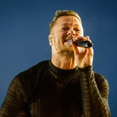 Wokalista Imagine Dragons na koncercie, z mikrofonem w dłoni, śpiewa z pasją.