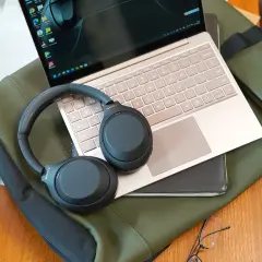 Słuchawki Sony na laptopie i zielonej torbie. Dowiedz się, jak włączyć słuchawki bezprzewodowe, by cieszyć się dźwiękiem.