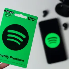 Karta podarunkowa Spotify Premium na 6 miesięcy kosztuje 120 zł. Obok leży smartfon z logo Spotify i słuchawki.