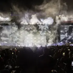 Koncert Linkin Park Polska na Open'er Festival. Tłum ludzi z telefonami, dym i światła na scenie.