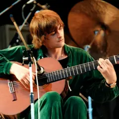 Mężczyzna w zielonym dresie gra na gitarze, a jego twarz skrywa się w **moonlight shadow**.