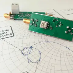 Elektroniczne moduły z pozłacanymi złączami leżą na wykresie Smitha, analizującym impedancję.