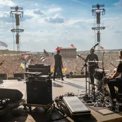 Zespół gra na scenie festiwalowej, tłum szaleje. W tle widać flagi, w tym z napisem "Sztywny Pal Azji utwory".