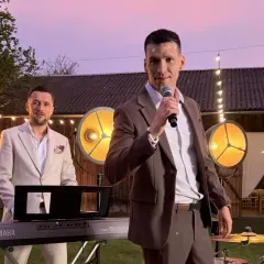 Zespół Defis gotowy do występu na świeżym powietrzu. Wokalista z mikrofonem, klawiszowiec przy keyboardzie, a w tle światła i budynek.