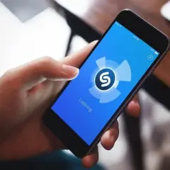 Dłoń trzyma smartfon z aplikacją Shazam, która analizuje dźwięk. Zastanawiasz się, jaka to piosenka?