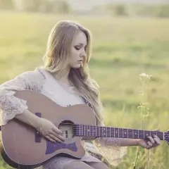 Piękny remaster: młoda kobieta z długimi blond włosami gra na gitarze akustycznej w słonecznym polu.