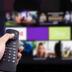 Dłoń trzyma pilot, wybierając program. Zastanawiasz się, kto jest zwolniony z abonamentu RTV? Może Ty?