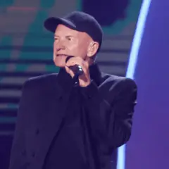 Sting w czapce i czarnym stroju śpiewa do mikrofonu. Ciekawe, ile Sting bierze za koncert, gdy występuje na tak dużej scenie.