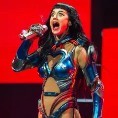 Katy Perry w błyszczącym, niebiesko-srebrnym kostiumie z sercem na piersi śpiewa na scenie w Krakowie.