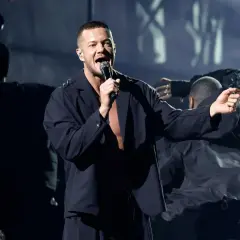 Imagine Dragons koncert Polska: wokalista Dan Reynolds śpiewa na scenie, otoczony tancerzami w mrocznej atmosferze.