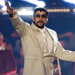 Bad Bunny koncert: artysta w beżowym garniturze z mikrofonem w dłoni, na scenie z tłumem w tle.