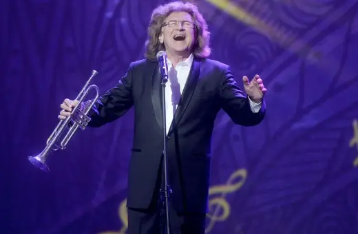 Zbigniew Wodecki w garniturze, z trąbką w dłoni, śpiewa na scenie. Jego utwory wciąż poruszają serca.