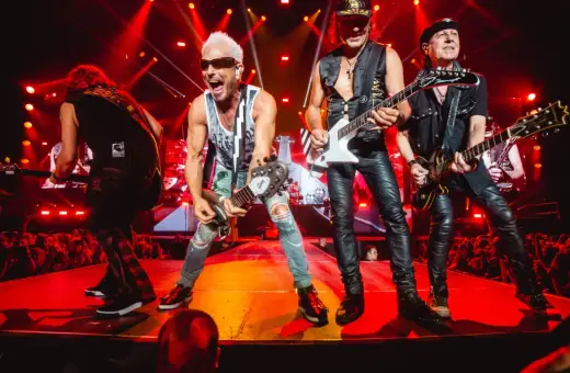 Scorpions na żywo, grając swoje legendarne utwory. Energetyczny koncert z czerwonymi światłami i tłumem fanów.