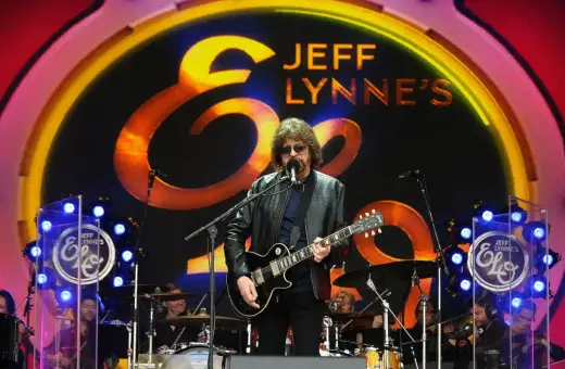 Jeff Lynne z Electric Light Orchestra na scenie, wykonuje swoje kultowe utwory. W tle logo zespołu.