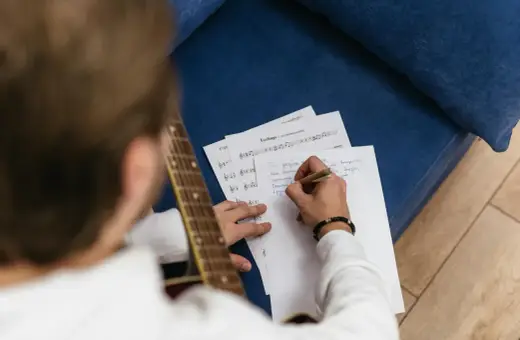 Mężczyzna z gitarą pisze tekst piosenki, tworząc nową wersję melodii.