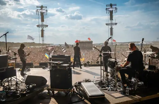 Zespół gra na scenie festiwalowej, tłum szaleje. W tle widać flagi, w tym z napisem "Sztywny Pal Azji utwory".