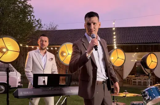 Zespół Defis gotowy do występu na świeżym powietrzu. Wokalista z mikrofonem, klawiszowiec przy keyboardzie, a w tle światła i budynek.
