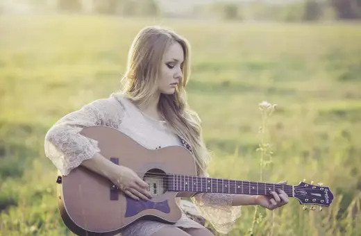 Piękny remaster: młoda kobieta z długimi blond włosami gra na gitarze akustycznej w słonecznym polu.