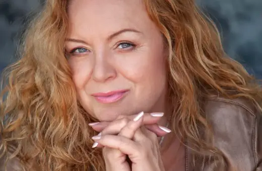 Hanna Banaszak z rudymi włosami i niebieskimi oczami, wpatrzona w obiektyw, jakby opowiadała historie zawarte w swoich utworach.