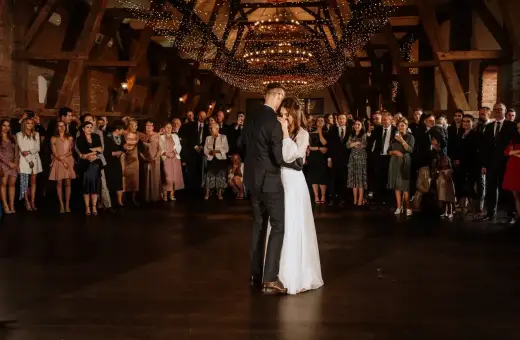 Para młoda tańczy pierwszy taniec przy blasku świateł. Goście obserwują wzruszający moment, idealny do wyboru piosenki na pierwszy taniec.