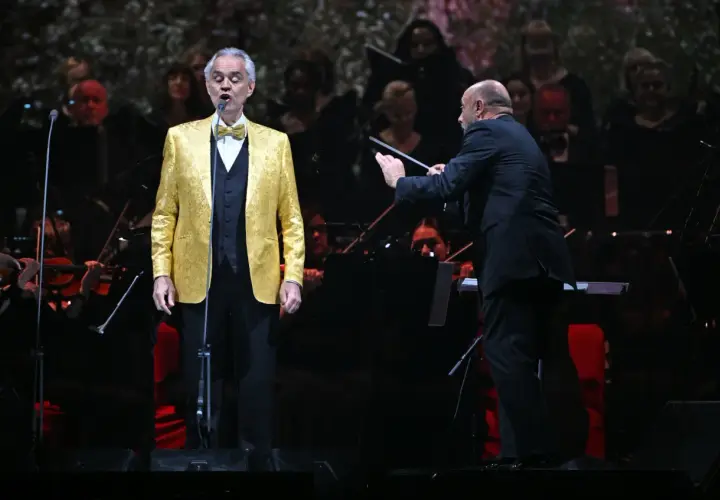 Andrea Bocelli w złotej marynarce śpiewa na scenie, dyrygent prowadzi orkiestrę. Koncert zapowiada się na niezapomniane przeżycie, jakiego można spodziewać się po Andrea Bocelli koncert 2026.