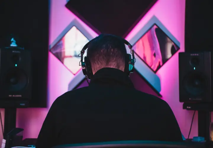 DJ w słuchawkach tworzy taneczne hity wszechczasów w studiu z neonowym oświetleniem.