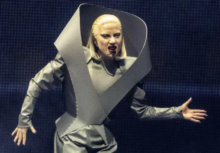 Lady Gaga w szarym, futurystycznym stroju na koncercie w Polsce, z charakterystycznym kołnierzem i makijażem.
