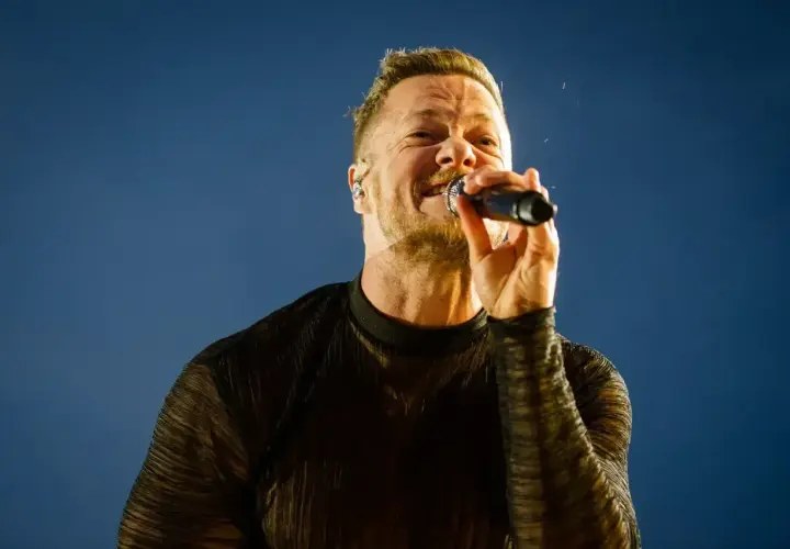 Wokalista Imagine Dragons na koncercie, z mikrofonem w dłoni, śpiewa z pasją.