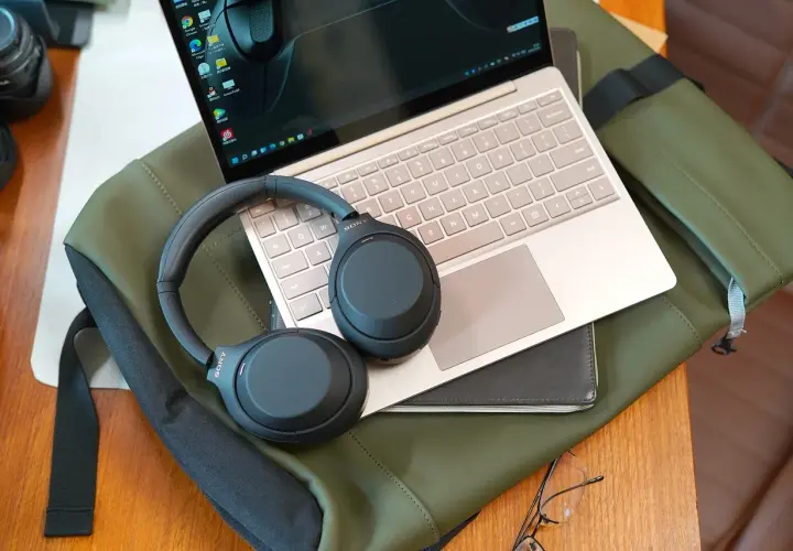 Słuchawki Sony na laptopie i zielonej torbie. Dowiedz się, jak włączyć słuchawki bezprzewodowe, by cieszyć się dźwiękiem.