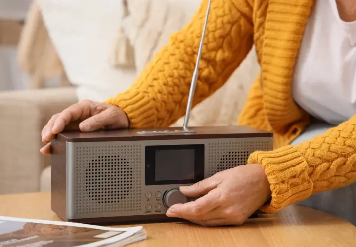 Dłoń kręci pokrętłem radia, by posłuchać RMF FM w pracy.