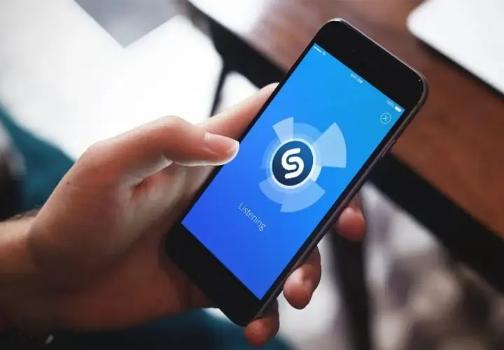 Dłoń trzyma smartfon z aplikacją Shazam, która analizuje dźwięk. Zastanawiasz się, jaka to piosenka?