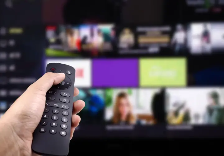 Dłoń trzyma pilot, wybierając program. Zastanawiasz się, kto jest zwolniony z abonamentu RTV? Może Ty?