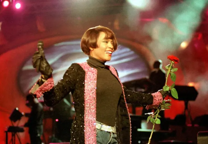 Whitney Houston w Polsce, na scenie z mikrofonem i czerwoną różą, w błyszczącej marynarce.