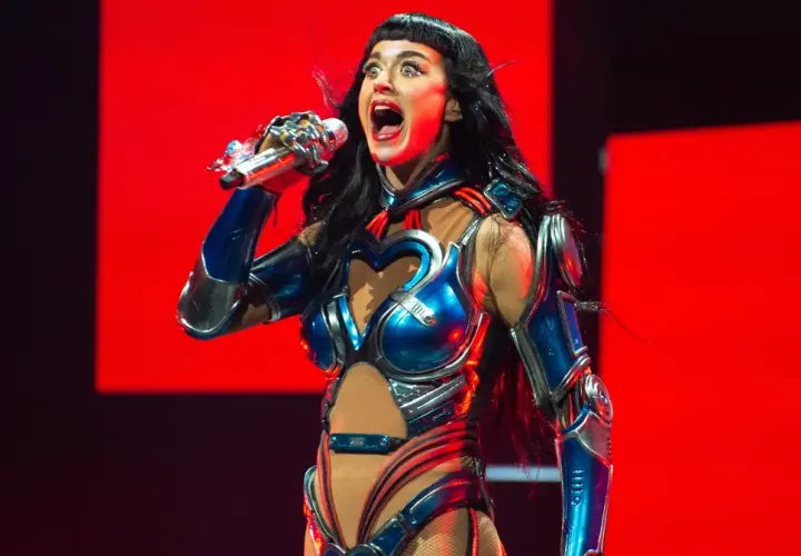Katy Perry w błyszczącym, niebiesko-srebrnym kostiumie z sercem na piersi śpiewa na scenie w Krakowie.
