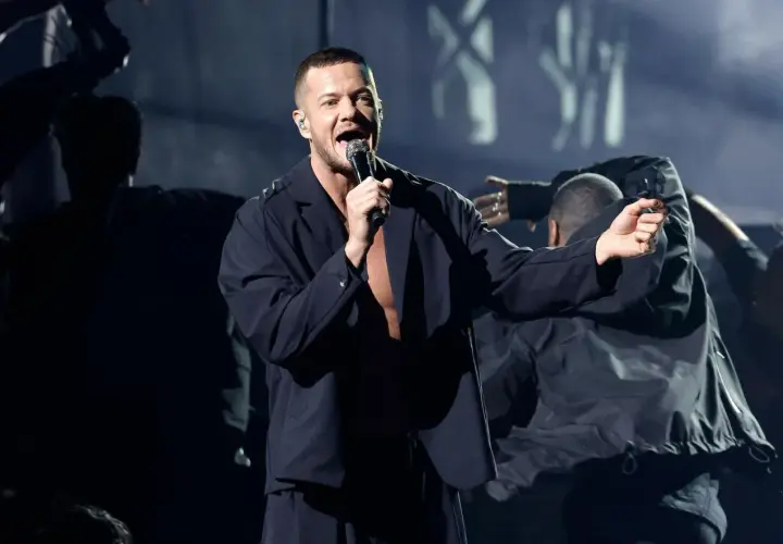 Imagine Dragons koncert Polska: wokalista Dan Reynolds śpiewa na scenie, otoczony tancerzami w mrocznej atmosferze.