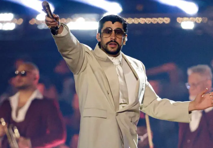 Bad Bunny koncert: artysta w beżowym garniturze z mikrofonem w dłoni, na scenie z tłumem w tle.