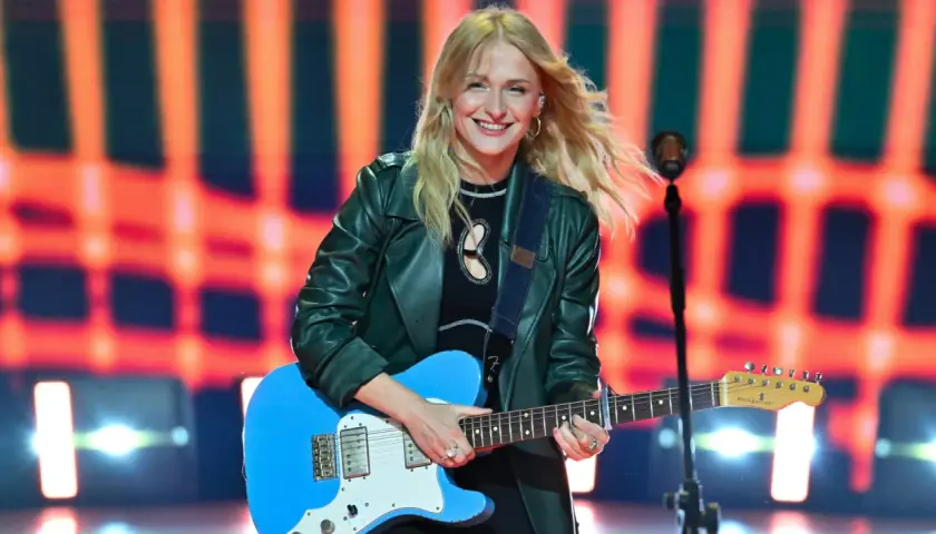Uśmiechnięta piosenkarka z blond włosami gra na niebieskiej gitarze. Jedna z wielu utalentowanych polskich piosenkarzy na scenie.