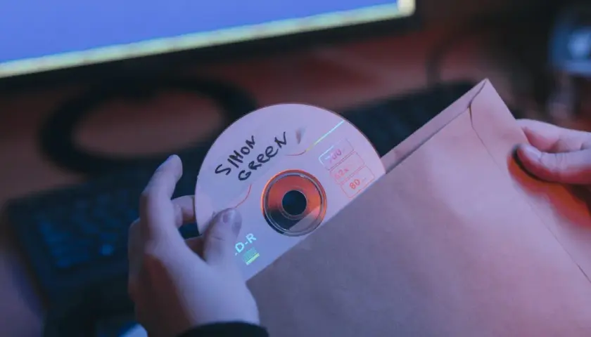 Ręce wsuwają płytę CD z napisem "Simon Green" do brązowej koperty. Może to być bootleg muzyczny.